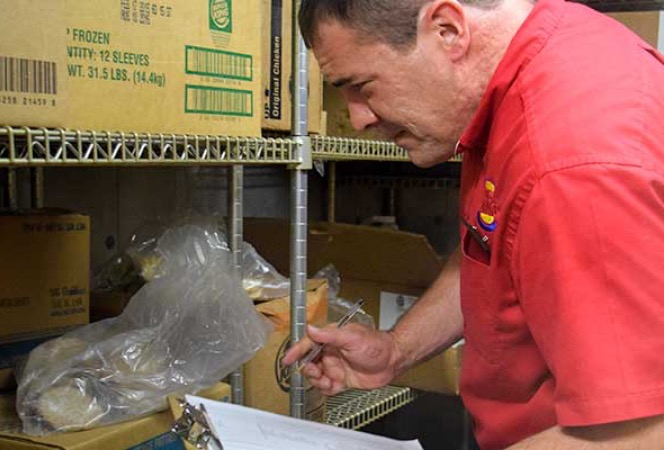 A male Burger King employee holding a clipboard examining inventory